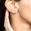 Close-up of a person wearing a diamond earring with a hand touching the earlobe.